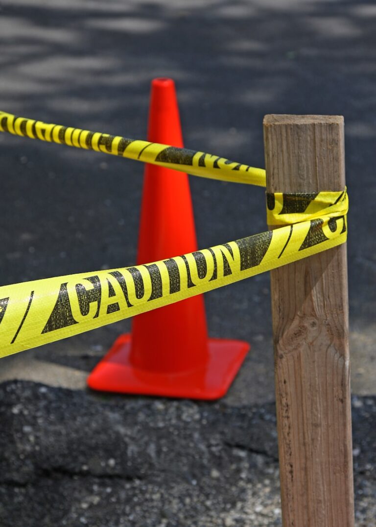 Yellow caution tape tied to wooden post, red cone.